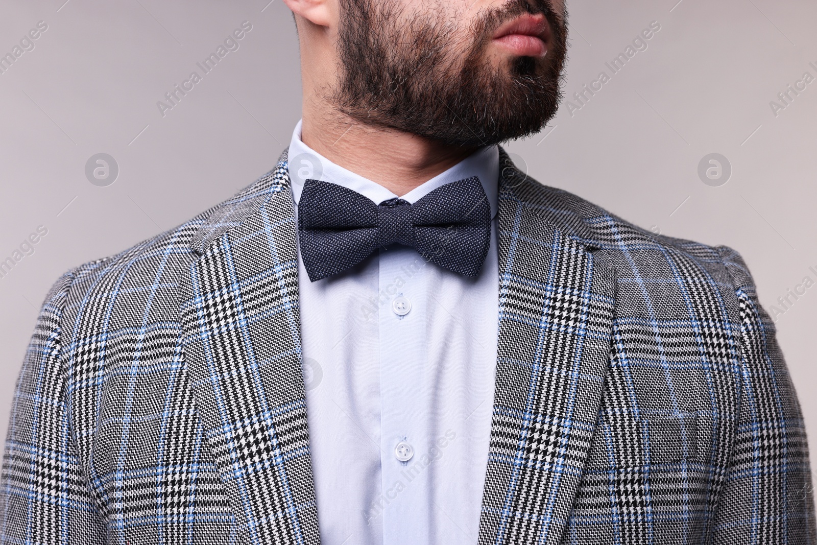 Photo of Man in suit, shirt and bow tie on grey background, closeup