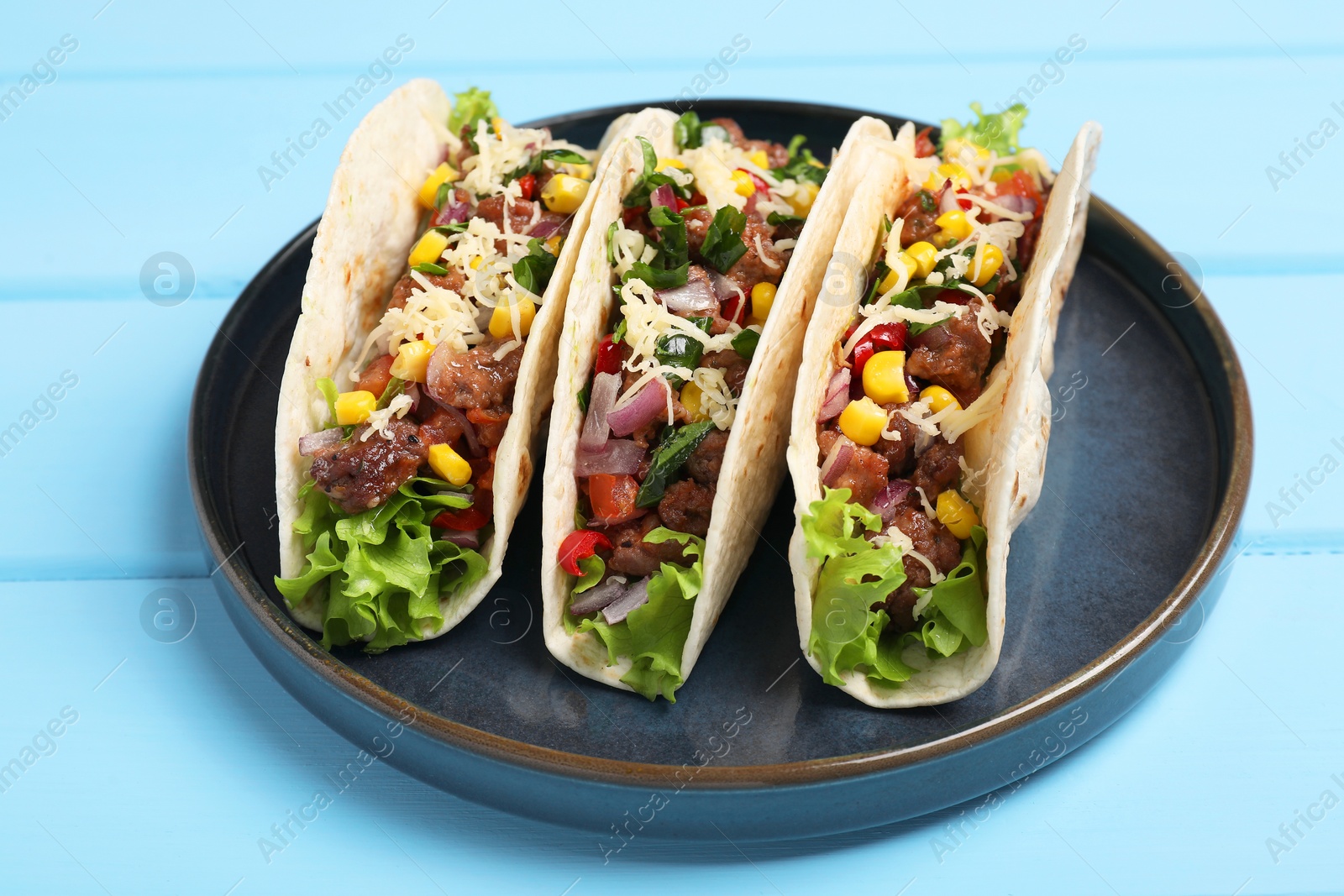 Photo of Delicious tacos with meat and vegetables on light blue table, closeup