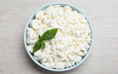 Photo of Fresh cottage cheese with basil in bowl on light wooden table, top view
