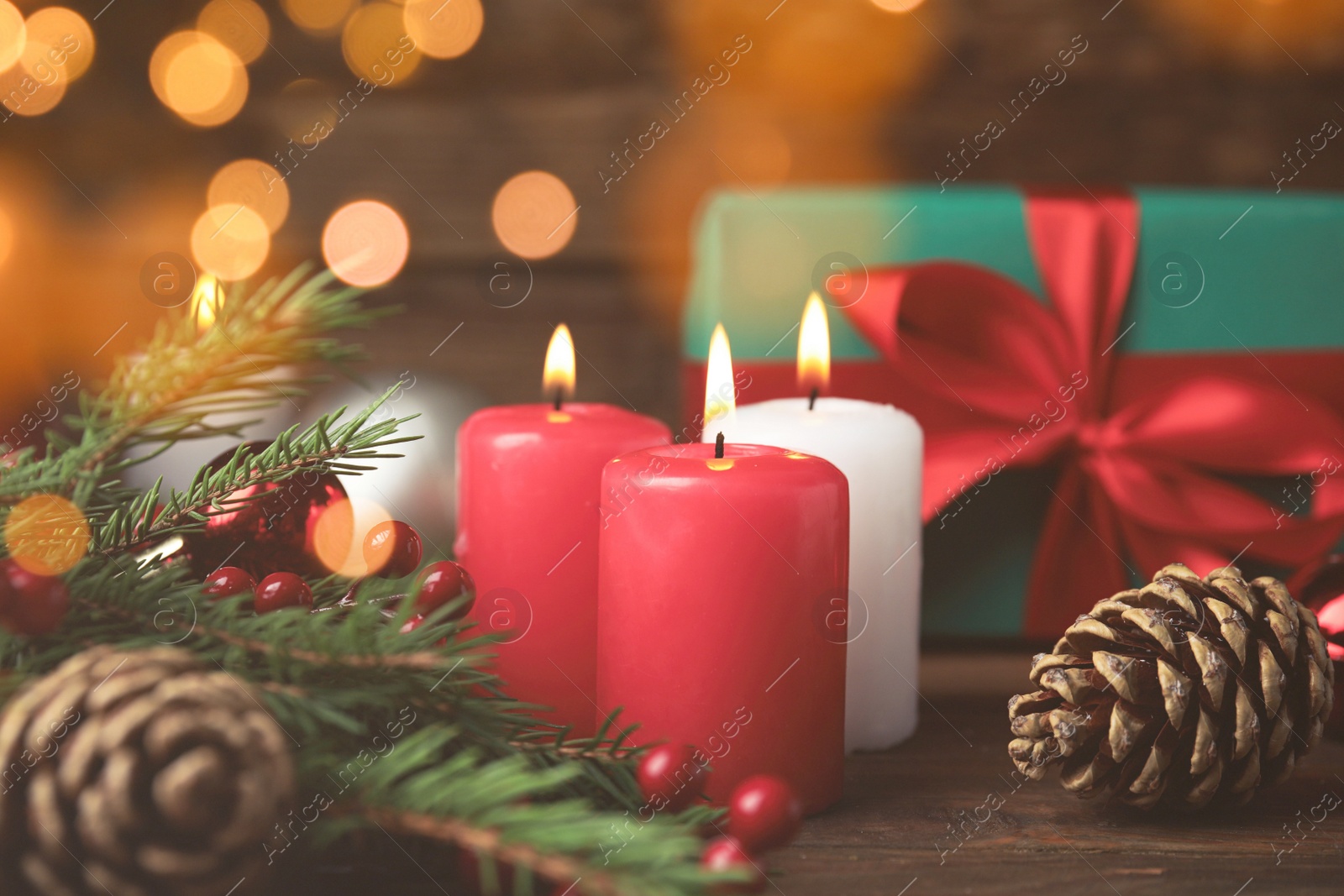 Photo of Burning candles, gift box and festive decor on wooden table, bokeh effect. Christmas eve