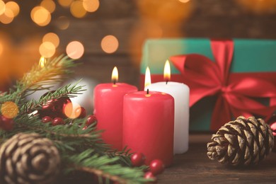 Photo of Burning candles, gift box and festive decor on wooden table, bokeh effect. Christmas eve