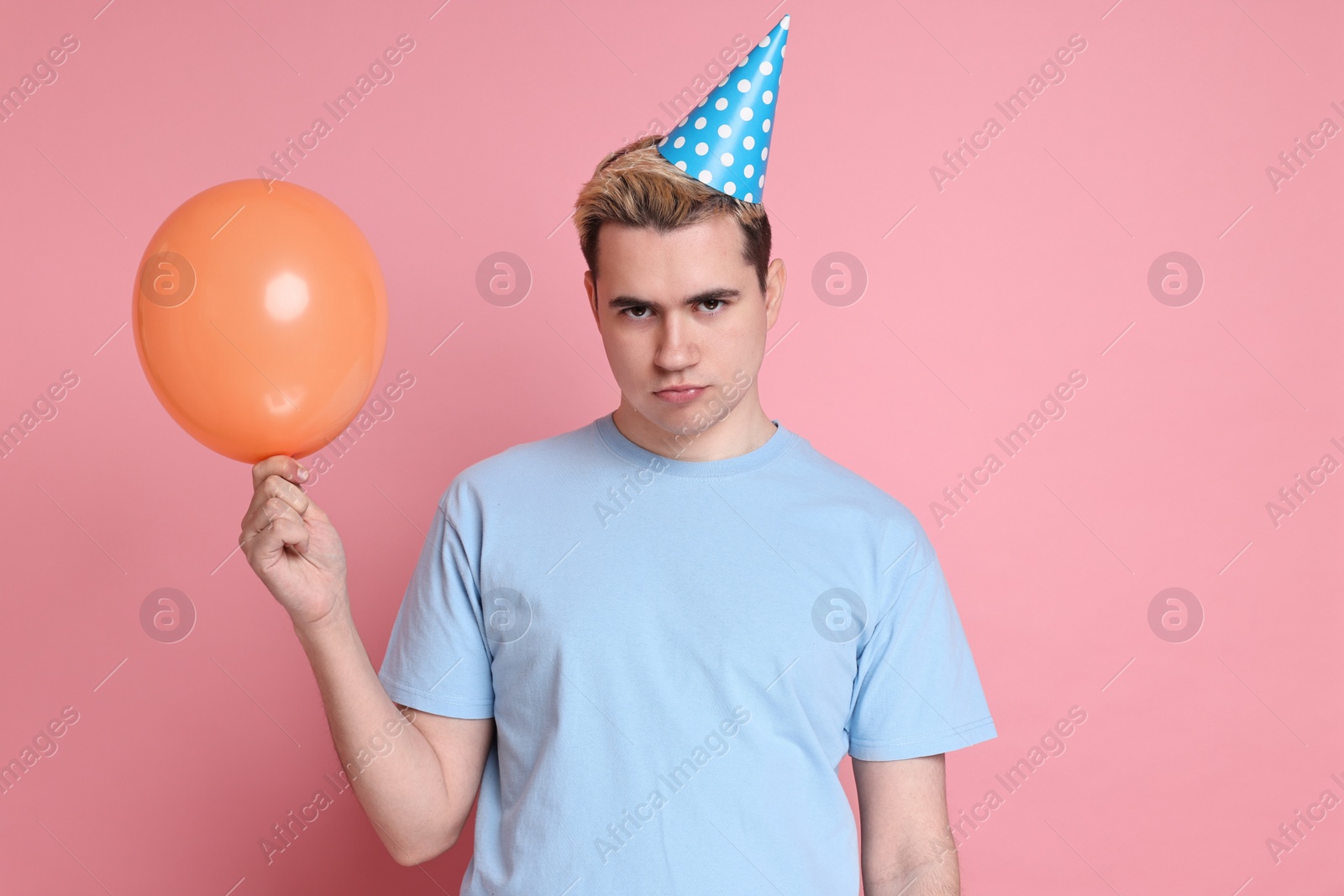 Photo of Sad young man with party hat and balloon on pink background