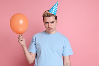 Sad young man with party hat and balloon on pink background