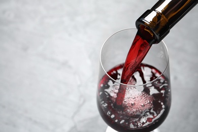 Pouring red wine from bottle into glass on light background, closeup. Space for text