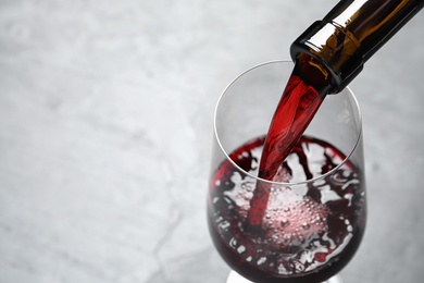 Photo of Pouring red wine from bottle into glass on light background, closeup. Space for text