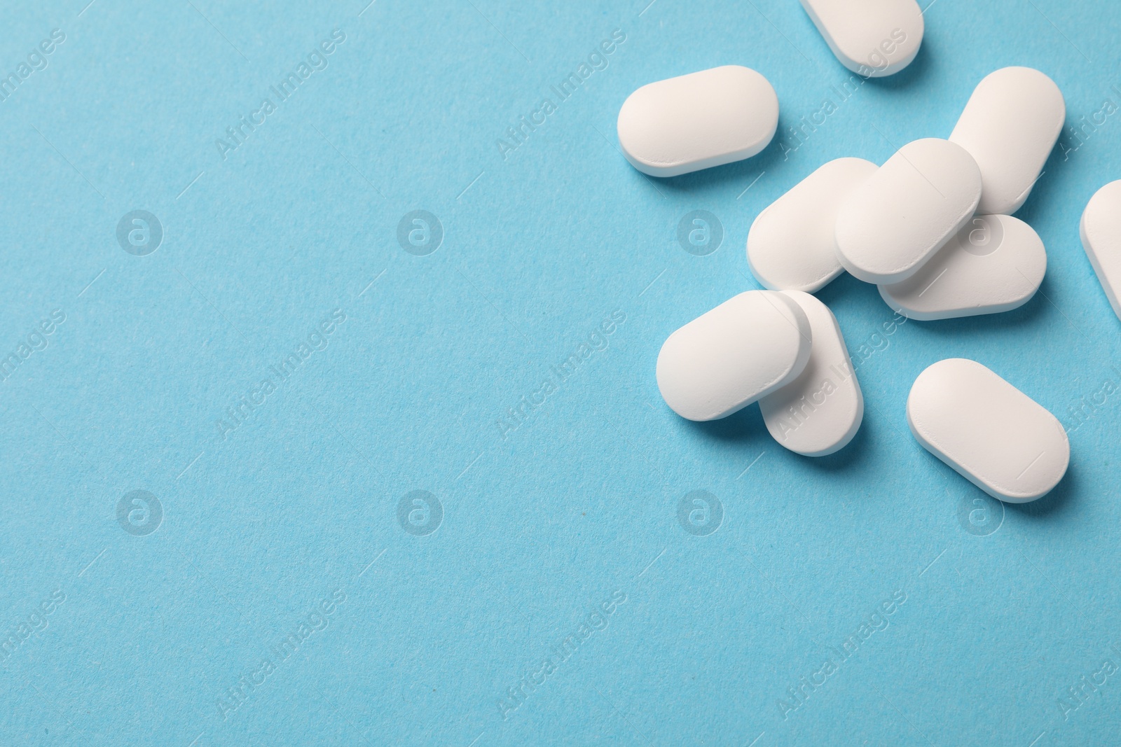 Photo of Pile of white pills on light blue background, flat lay. Space for text