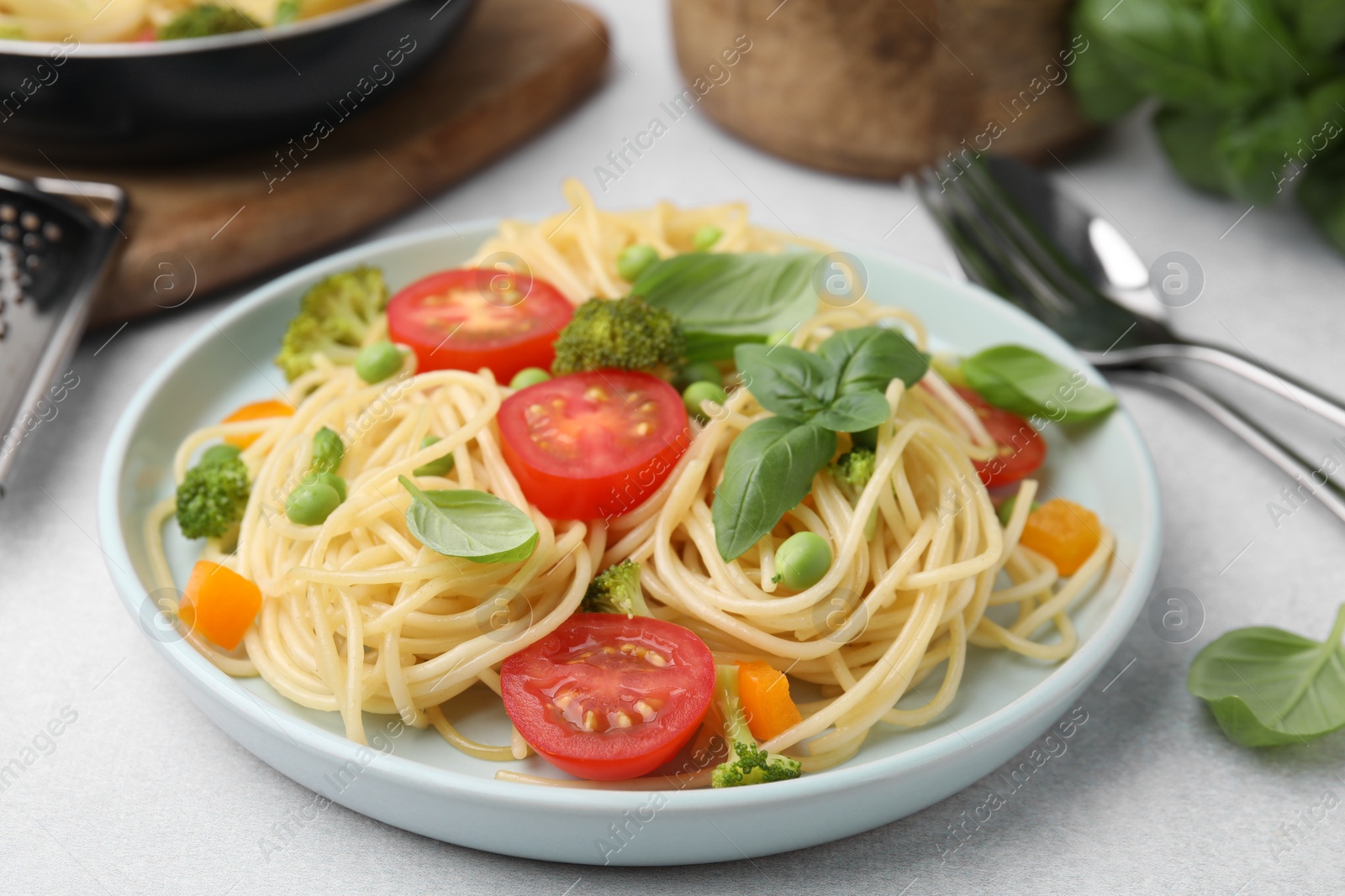 Photo of Delicious pasta primavera and cutlery on light gray table, closeup