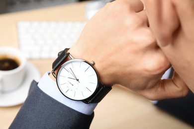 Businessman with wrist watch working at office table, closeup. Time management