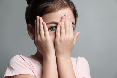 Photo of Little girl feeling fear on grey background, closeup