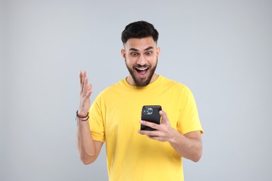 Photo of Happy young man using smartphone on grey background