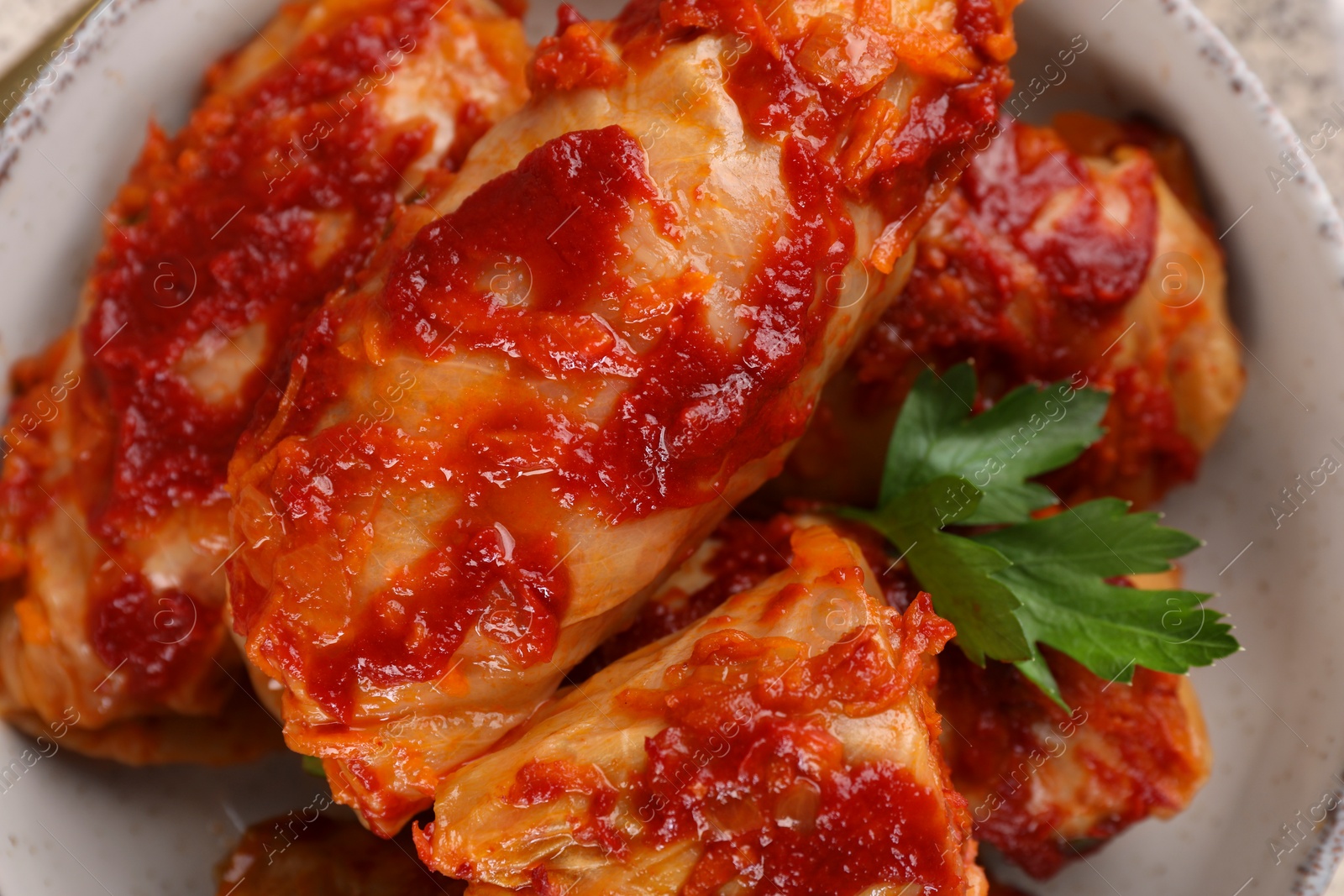 Photo of Delicious stuffed cabbage rolls cooked with homemade tomato sauce in bowl, top view