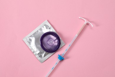 Contraception choice. Condoms and intrauterine device on pink background, flat lay