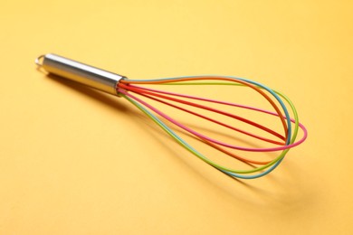 Photo of Bright whisk on yellow background, closeup. Kitchen tool