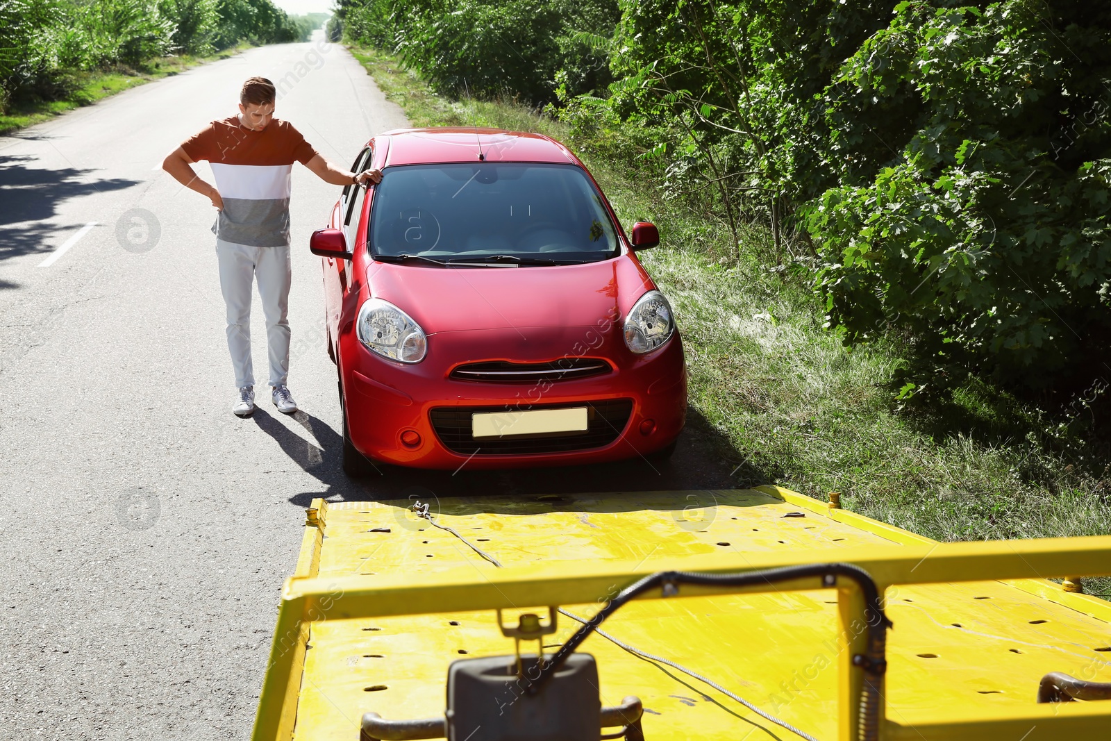 Photo of Man near broken car and tow truck on country road