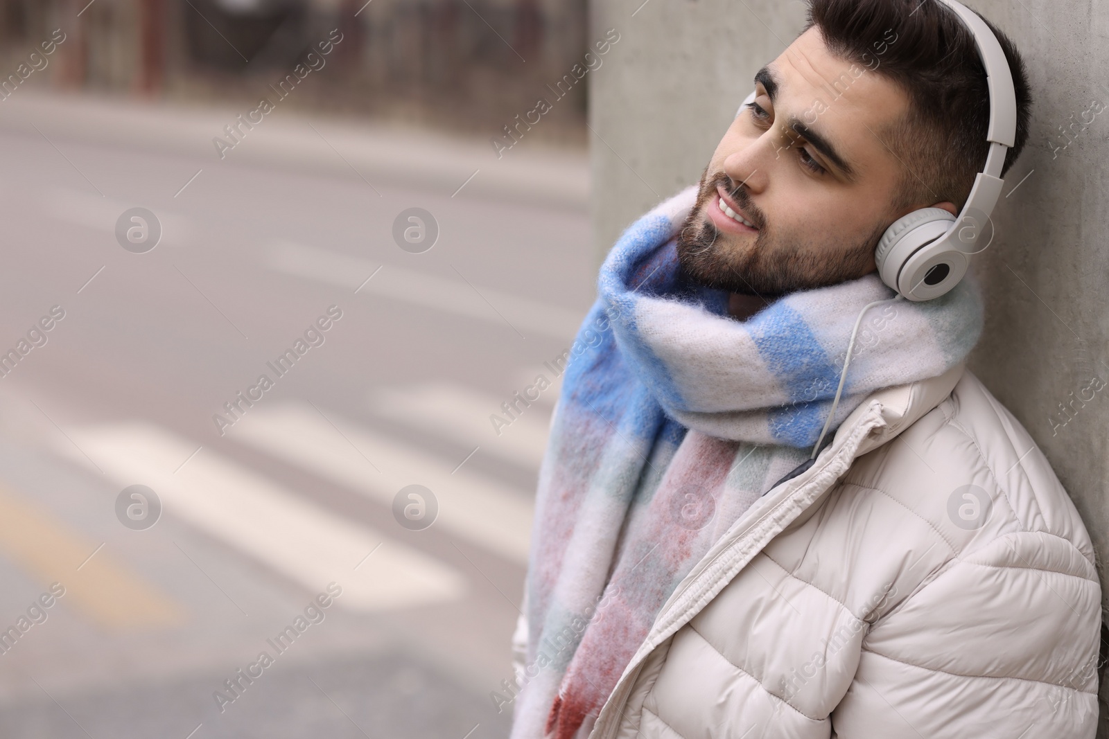 Photo of Smiling man in warm scarf and headphones on city street. Space for text