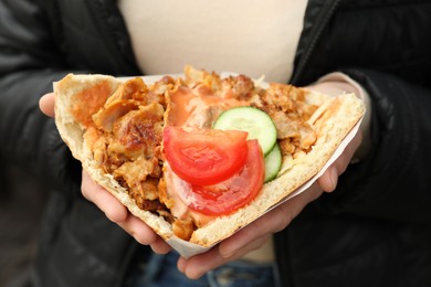 Photo of Woman holding delicious bread with roasted meat and vegetables, closeup. Street food