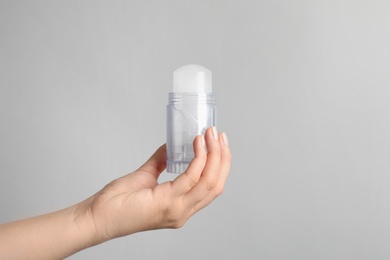 Photo of Young woman holding natural crystal alum deodorant on light grey background, closeup