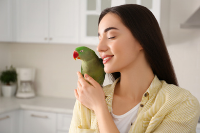 Photo of Young woman with Alexandrine parakeet indoors. Cute pet