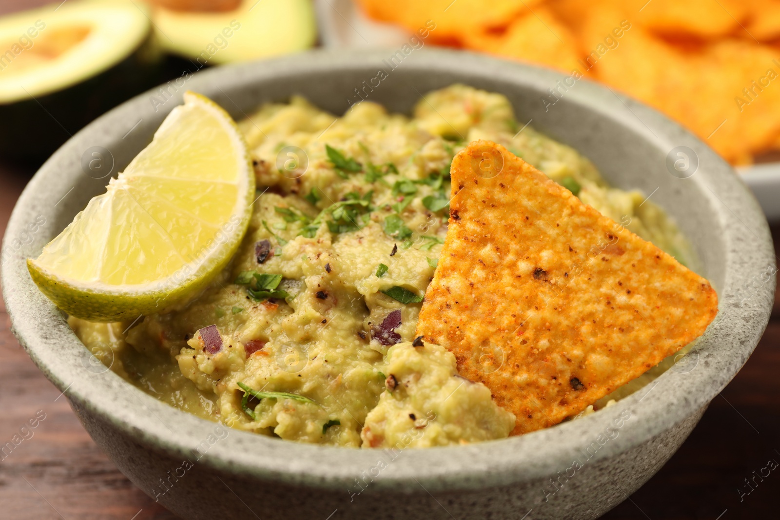 Photo of Bowl of delicious guacamole, lime and nachos chips on wooden table, closeup