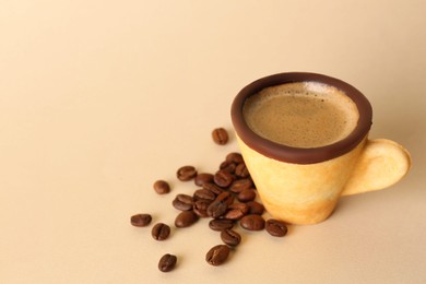 Delicious edible biscuit cup with espresso and coffee beans on beige background. Space for text