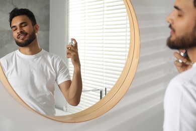 Man spraying luxury perfume near mirror indoors