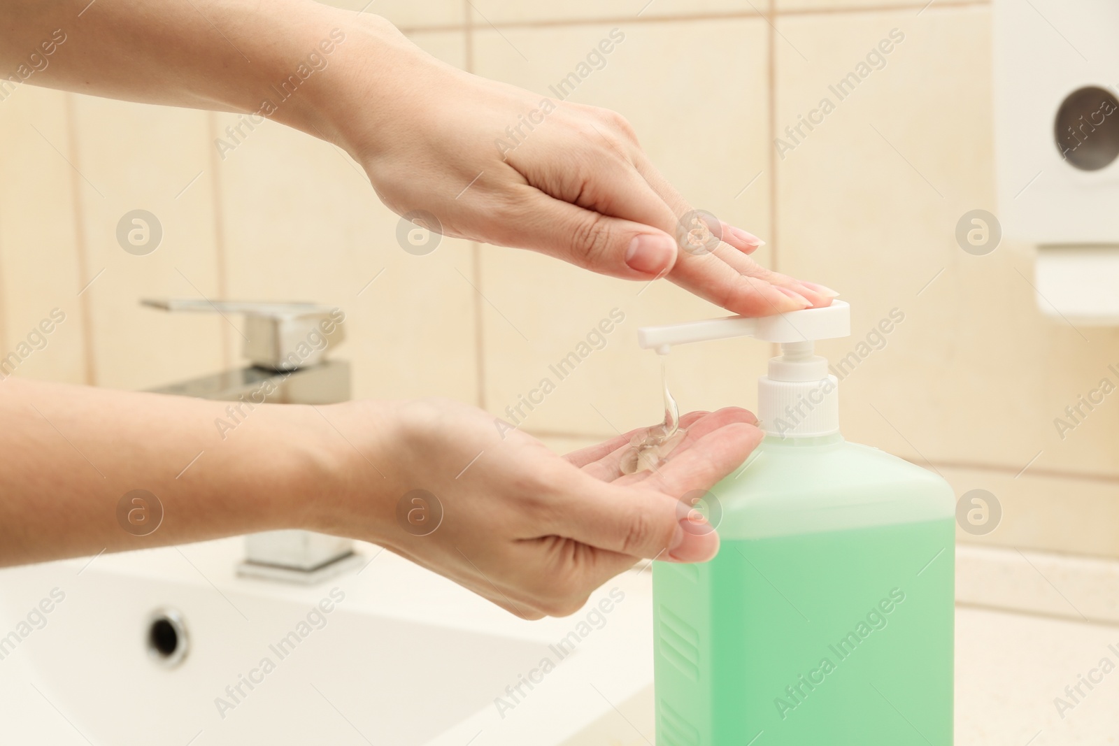 Photo of Woman applying antiseptic gel on hand in public bathroom, closeup