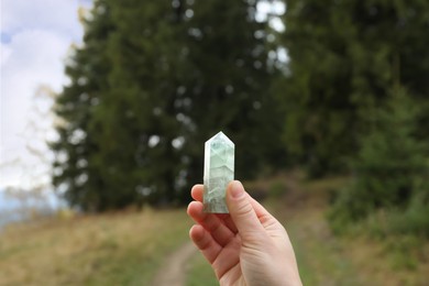 Photo of Woman holding beautiful crystal near forest, closeup