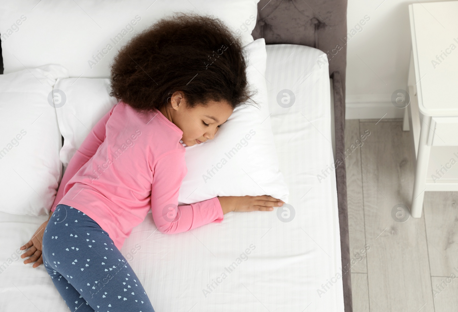 Photo of Cute little African-American girl sleeping in bed, top view