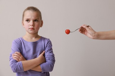 Cute little girl refusing to eat tomato on grey background
