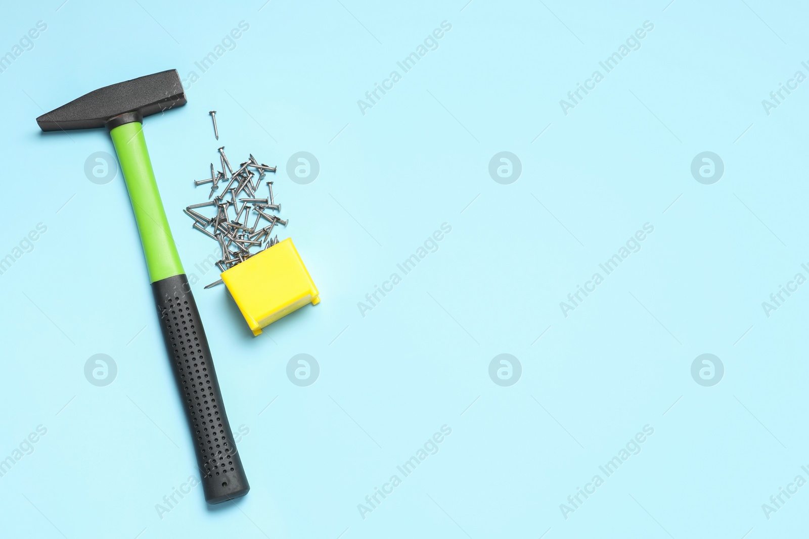 Photo of Hammer and metal nails on light blue background, flat lay. Space for text