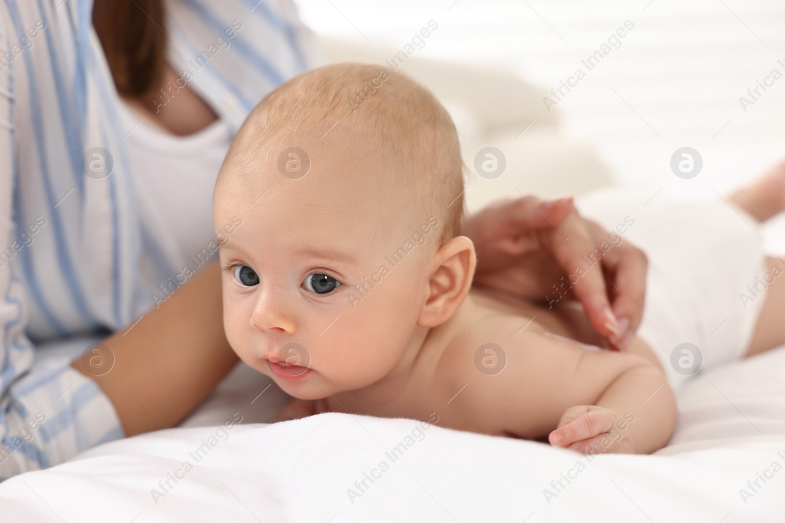 Photo of Woman applying body cream onto baby`s skin on bed, closeup