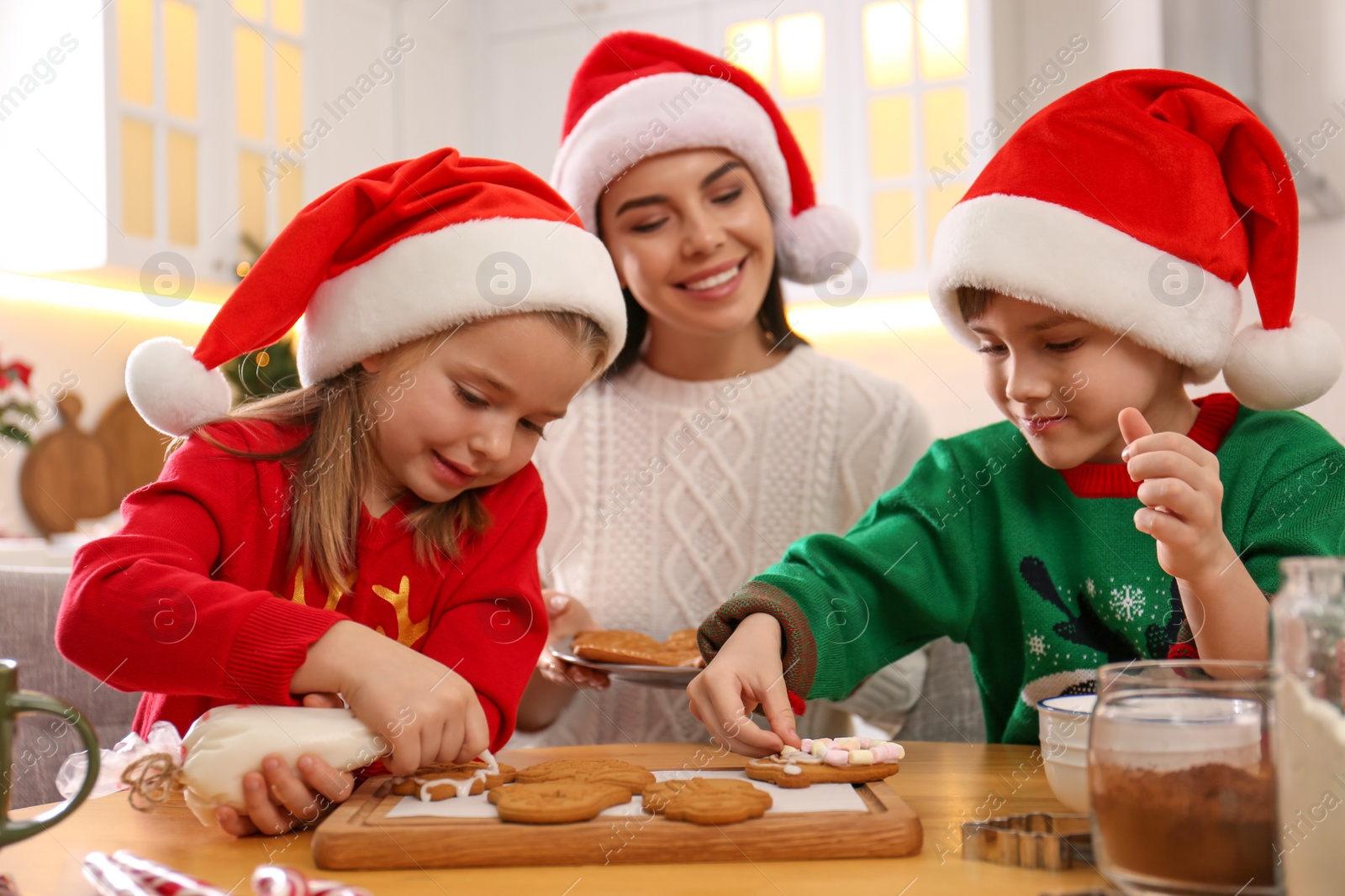 Photo of Mother and her cute little children decorating tasty Christmas cookies at table in kitchen