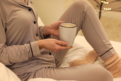 Woman in grey pajama holding cup of coffee indoors, closeup