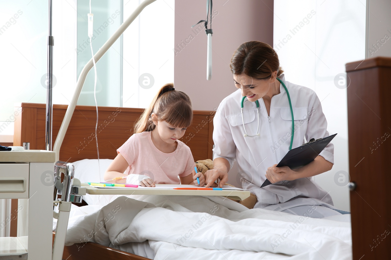 Photo of Little child with intravenous drip drawing in hospital bed during doctor's visit