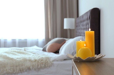 Photo of Burning candles on bedside table in bedroom