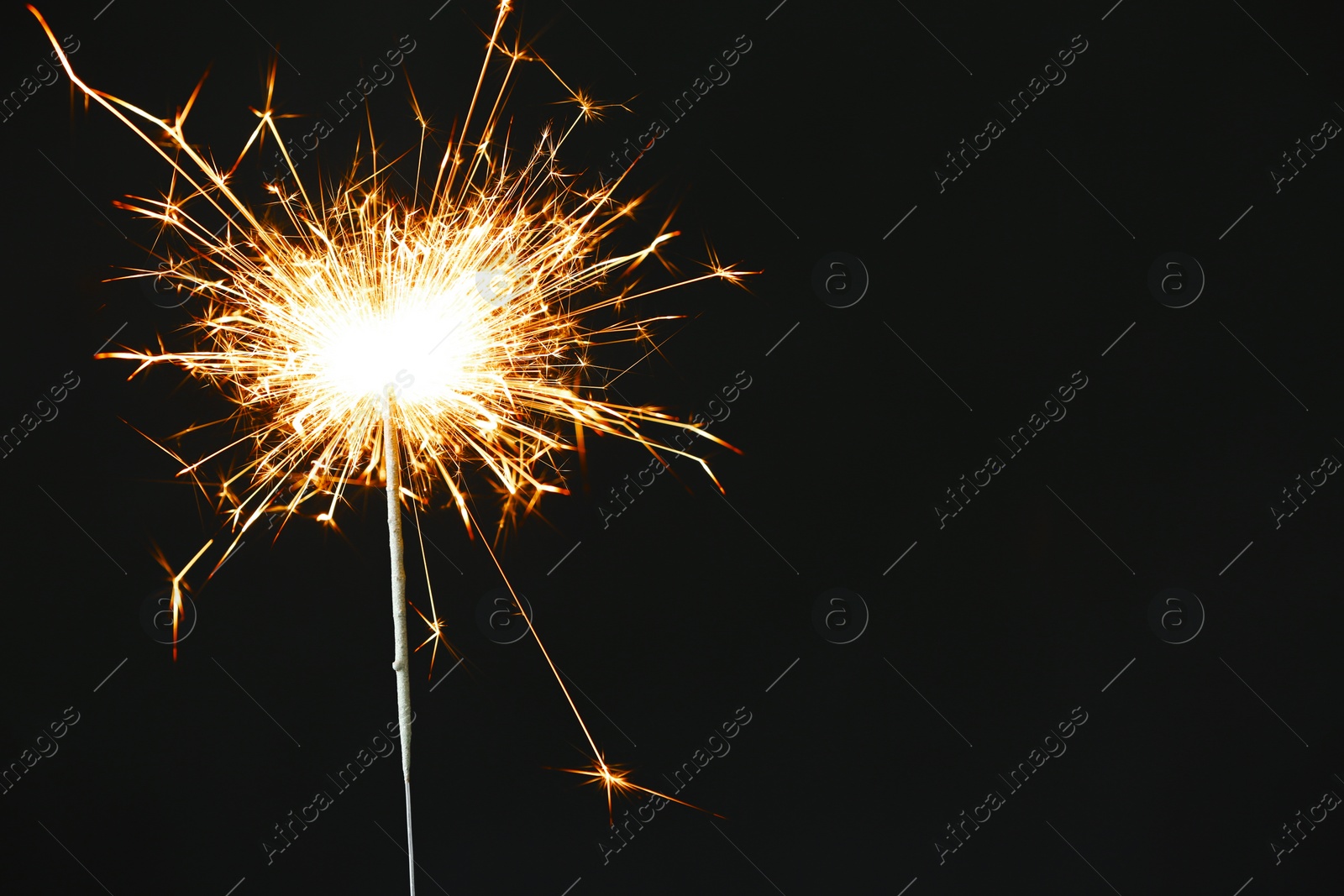 Photo of Bright burning sparkler on black background, closeup. Space for text