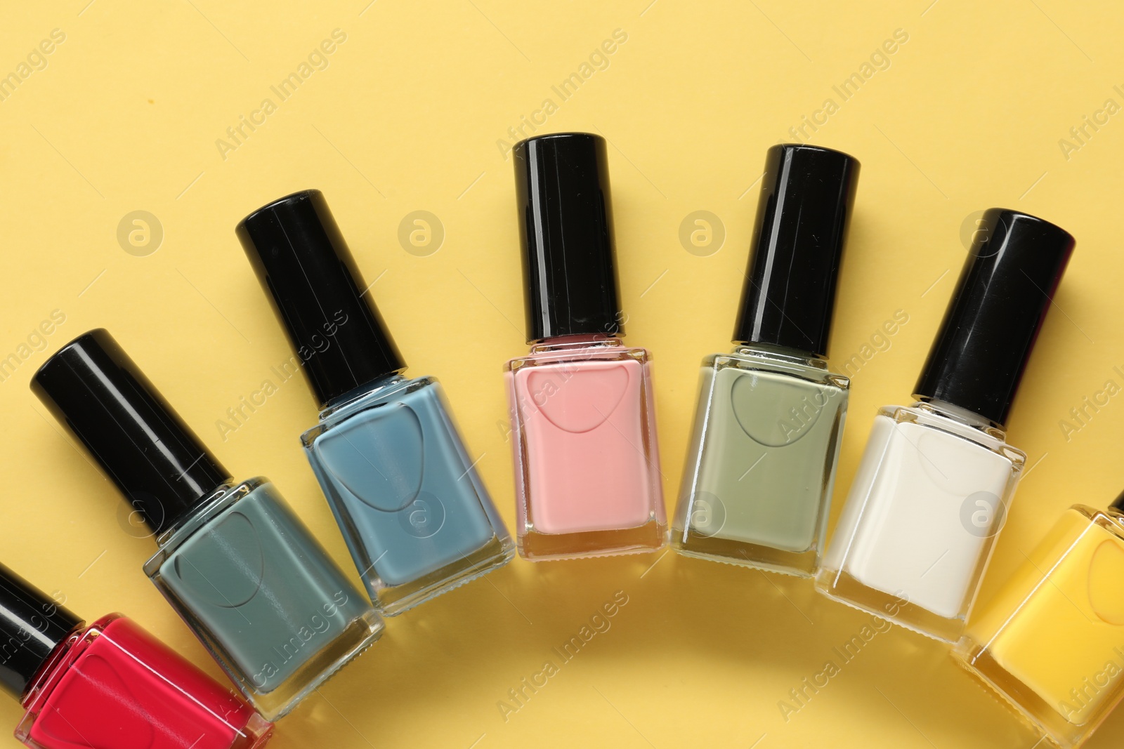 Photo of Colorful nail polishes in bottles on yellow background, flat lay