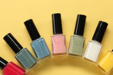 Colorful nail polishes in bottles on yellow background, flat lay