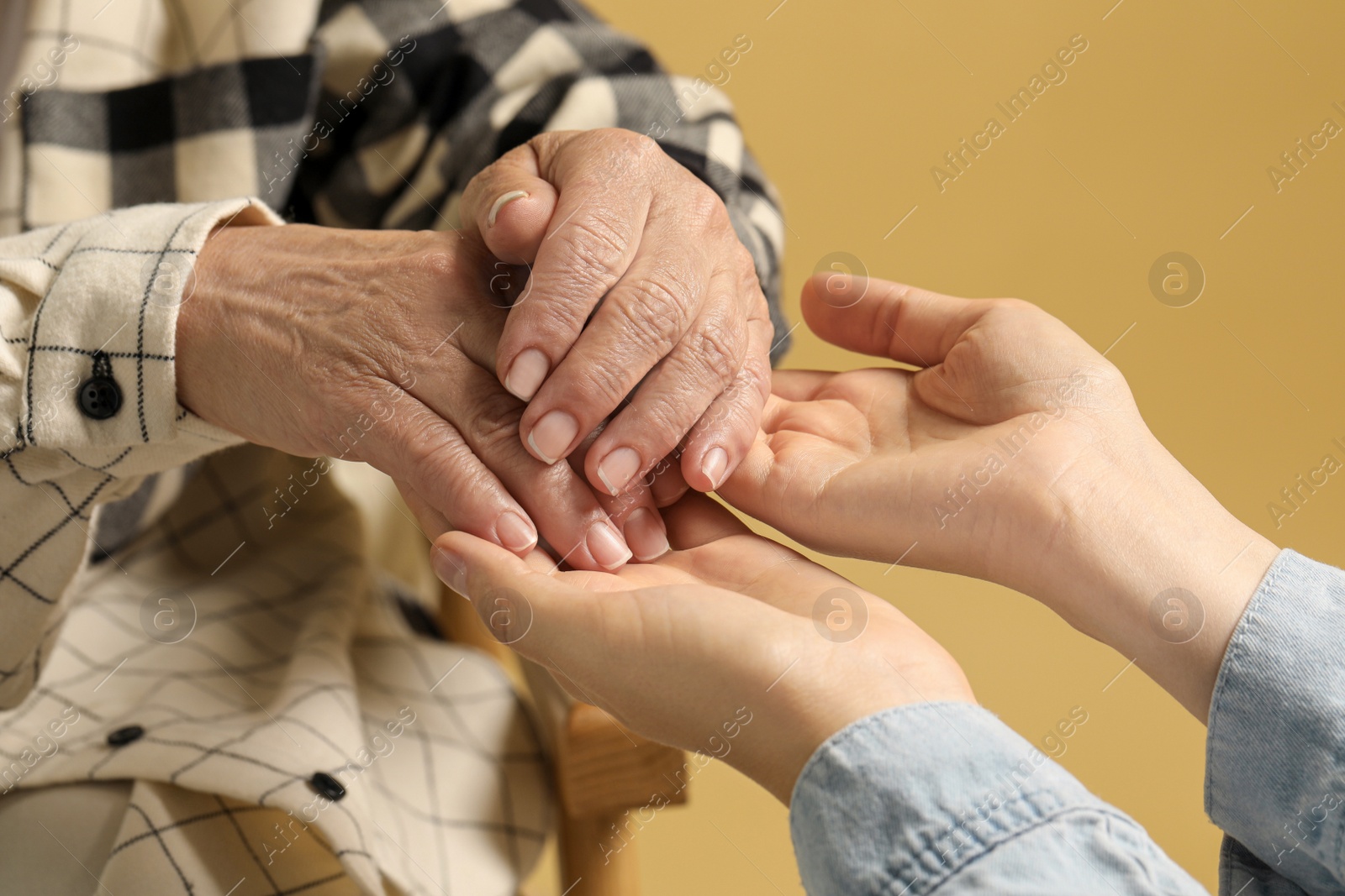 Photo of Young and elderly women holding hands on beige background, closeup