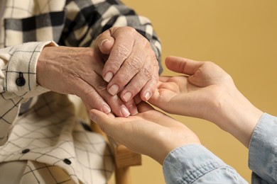 Young and elderly women holding hands on beige background, closeup