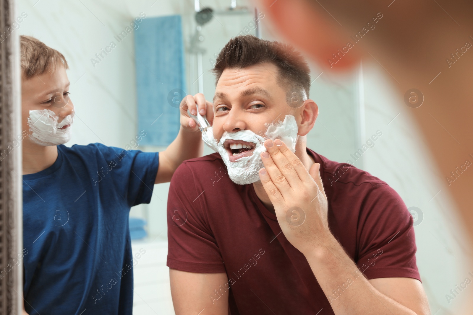 Photo of Son applying shaving foam on dad's face at mirror in bathroom