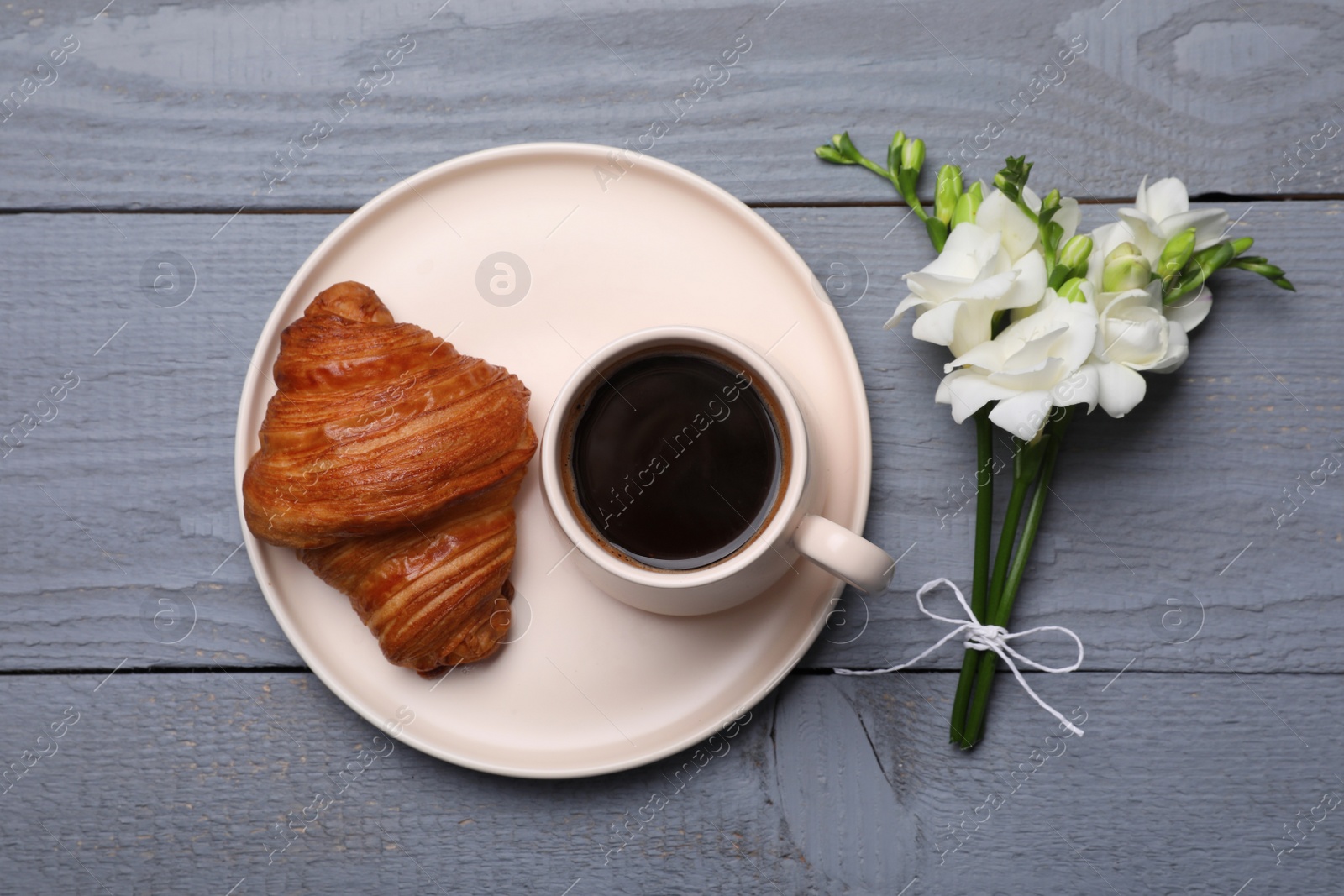 Photo of Aromatic morning coffee, croissant and flowers on grey wooden table, flat lay