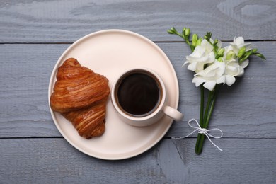 Aromatic morning coffee, croissant and flowers on grey wooden table, flat lay