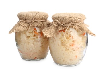 Glass jars of tasty fermented cabbage with carrot on white background