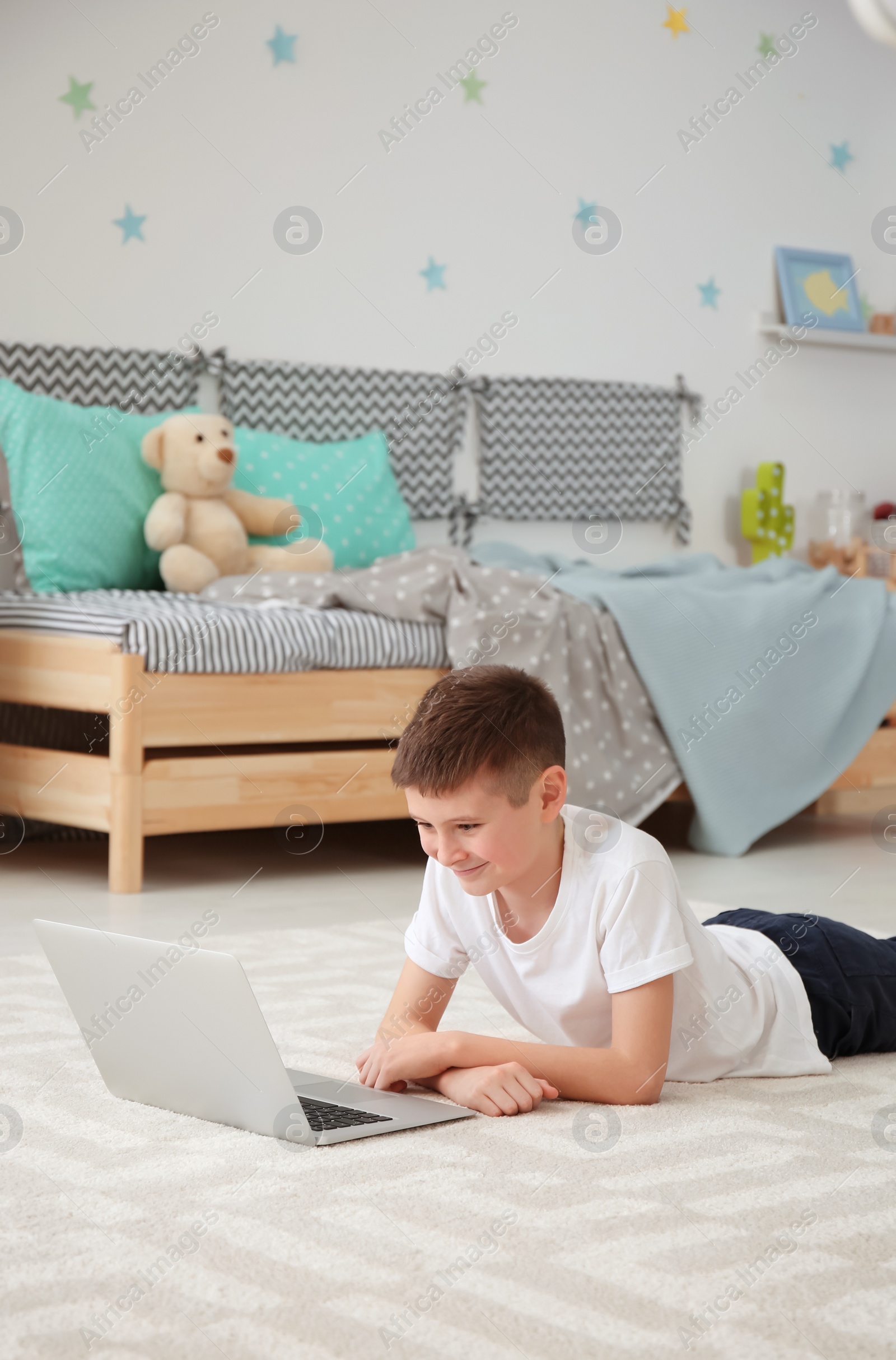 Photo of Happy boy with laptop lying on cozy carpet at home