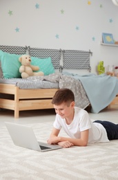 Happy boy with laptop lying on cozy carpet at home