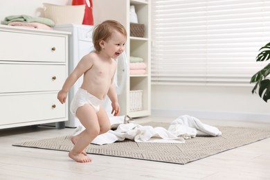 Little girl having fun near baby clothes indoors