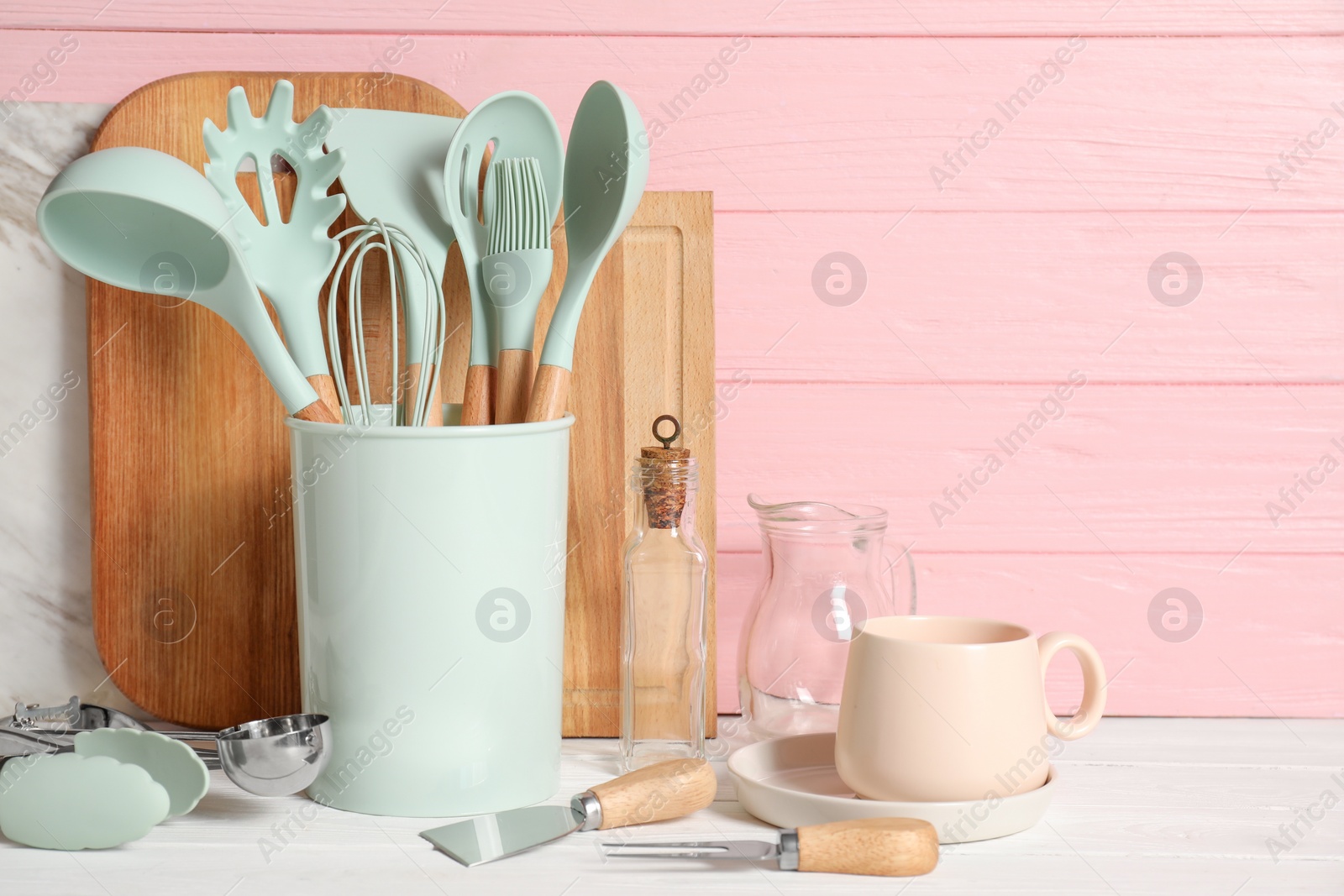 Photo of Set of different kitchen utensils on white table against pink wooden background, space for text