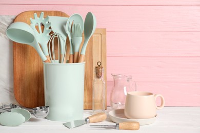 Set of different kitchen utensils on white table against pink wooden background, space for text