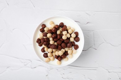 Photo of Breakfast cereal. Tasty corn balls with milk in bowl on white textured table, top view